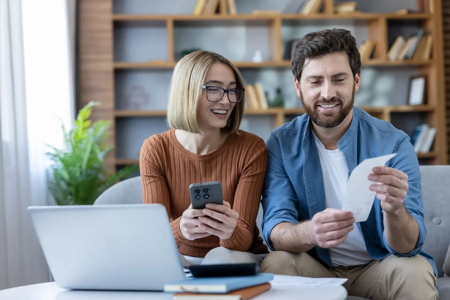 A smiling couple going over bills together at their laptop