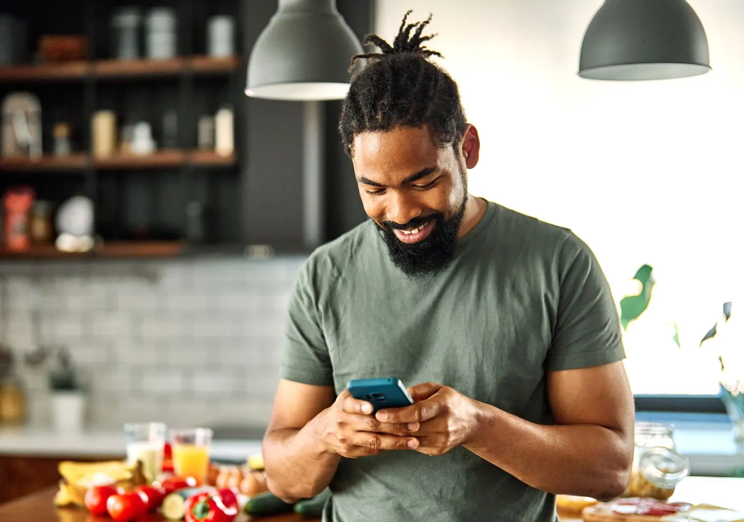 A smiling man looking up recipes on his phone in a bright kitchen