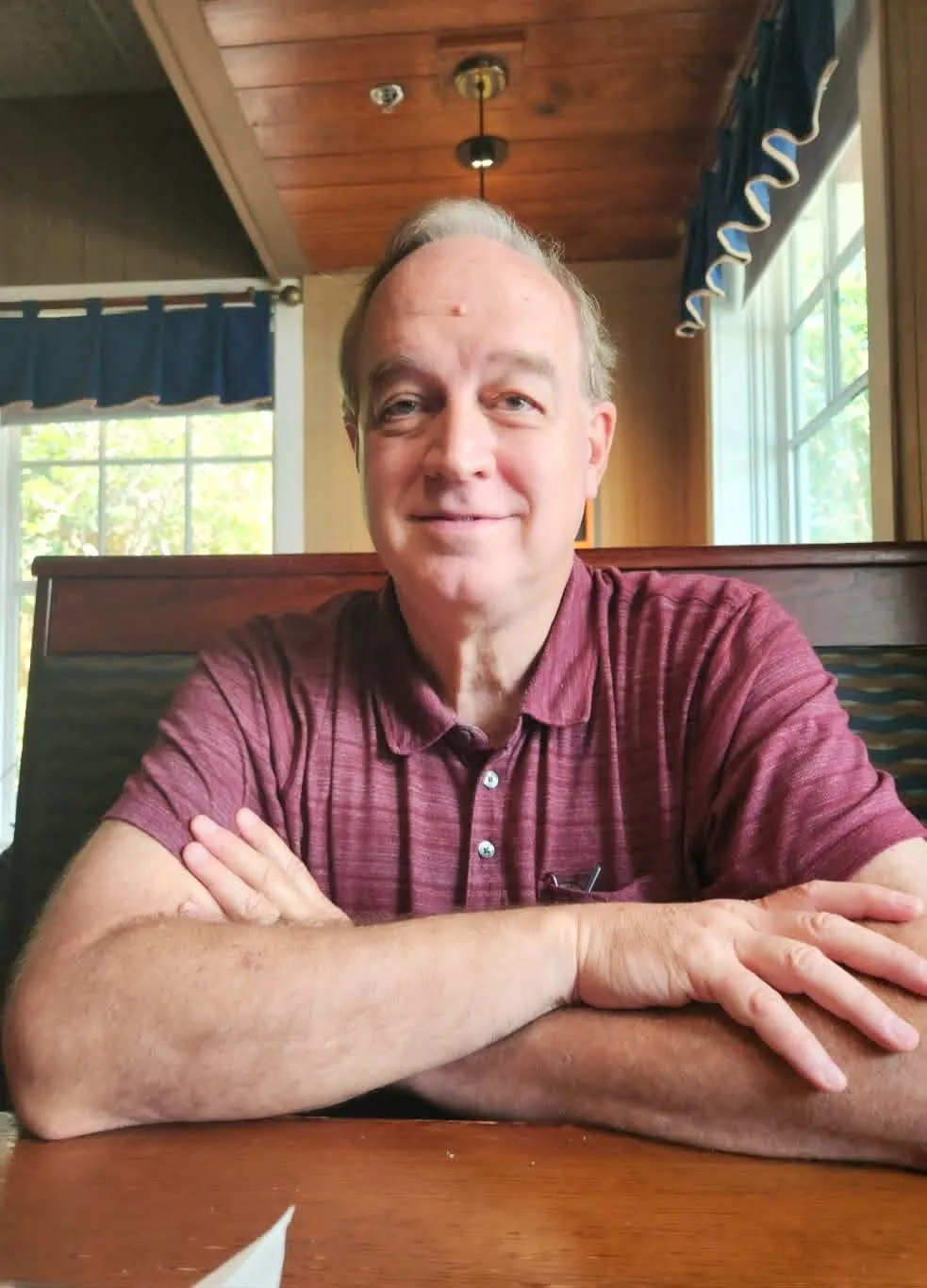 John Crapo, counselor, seated at a wooden table with his arms folded, smiling